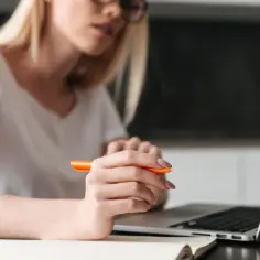 Kobieta w okularach pisze w notatniku, przygotowując przykładowe uzasadnienie wniosku o przyznanie pomocy zdrowotnej na okulary.